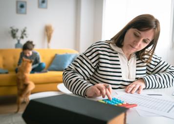 Woman managing the monthly family budget while her daughter plays with a dog in the background