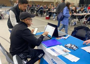 An OPA team member assists a borrower in applying for a 1% interest loan to pay for their citizenship fees at a community event.