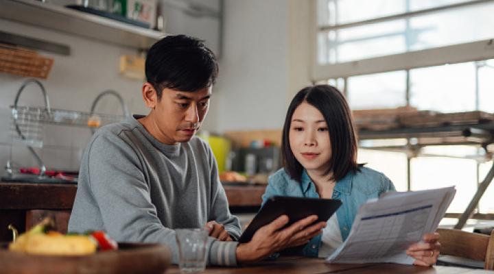 An Asian couple looks at a computer and has papers and receipts on their table